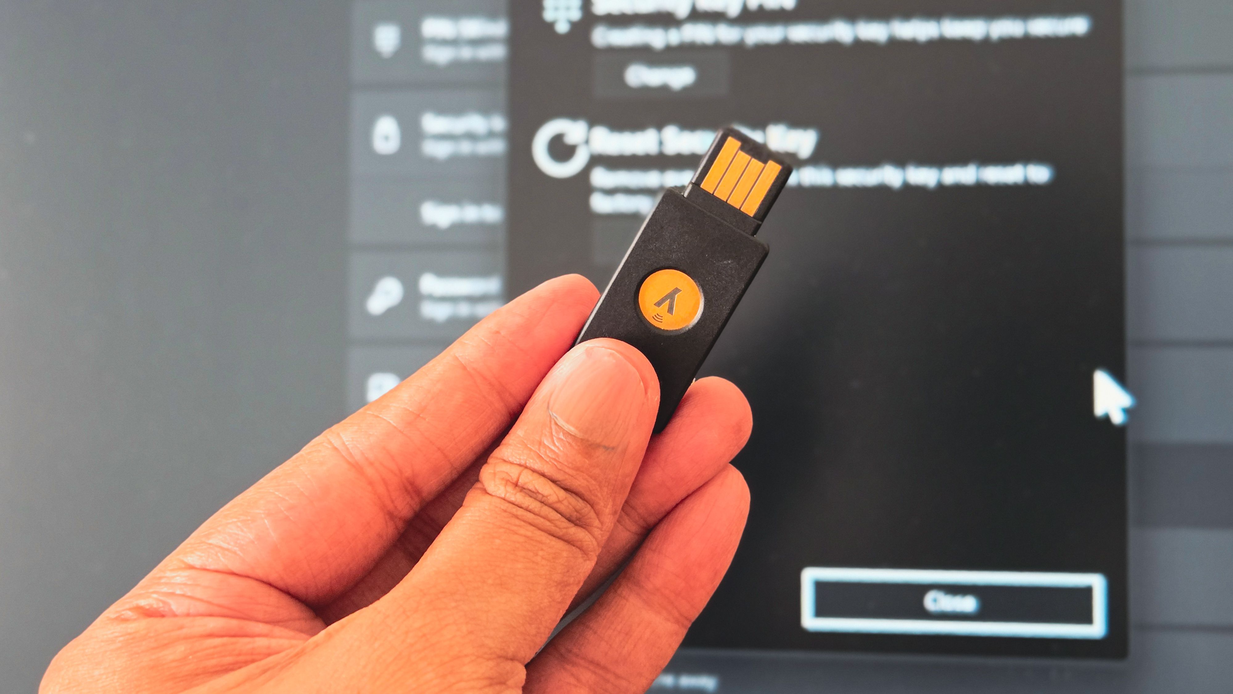 Person holding a YubiKey infront of a Windows 11 desktop monitor