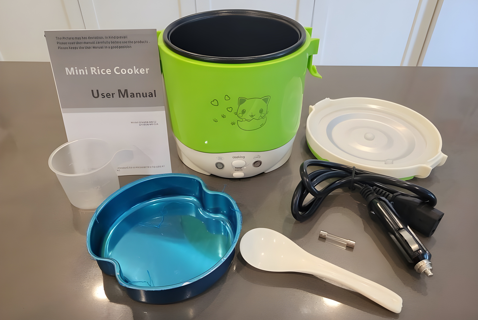 A mini rice cooker with accessories on a gray countertop.