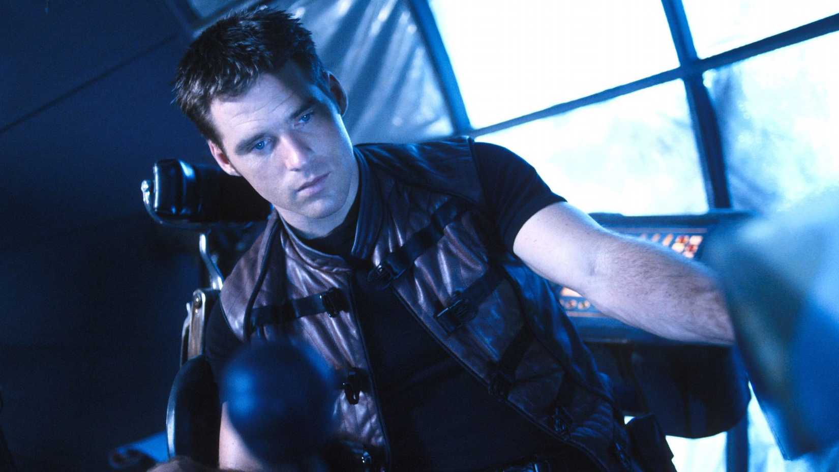 Ben Browder as John Crichton sitting at a console in Farscape.