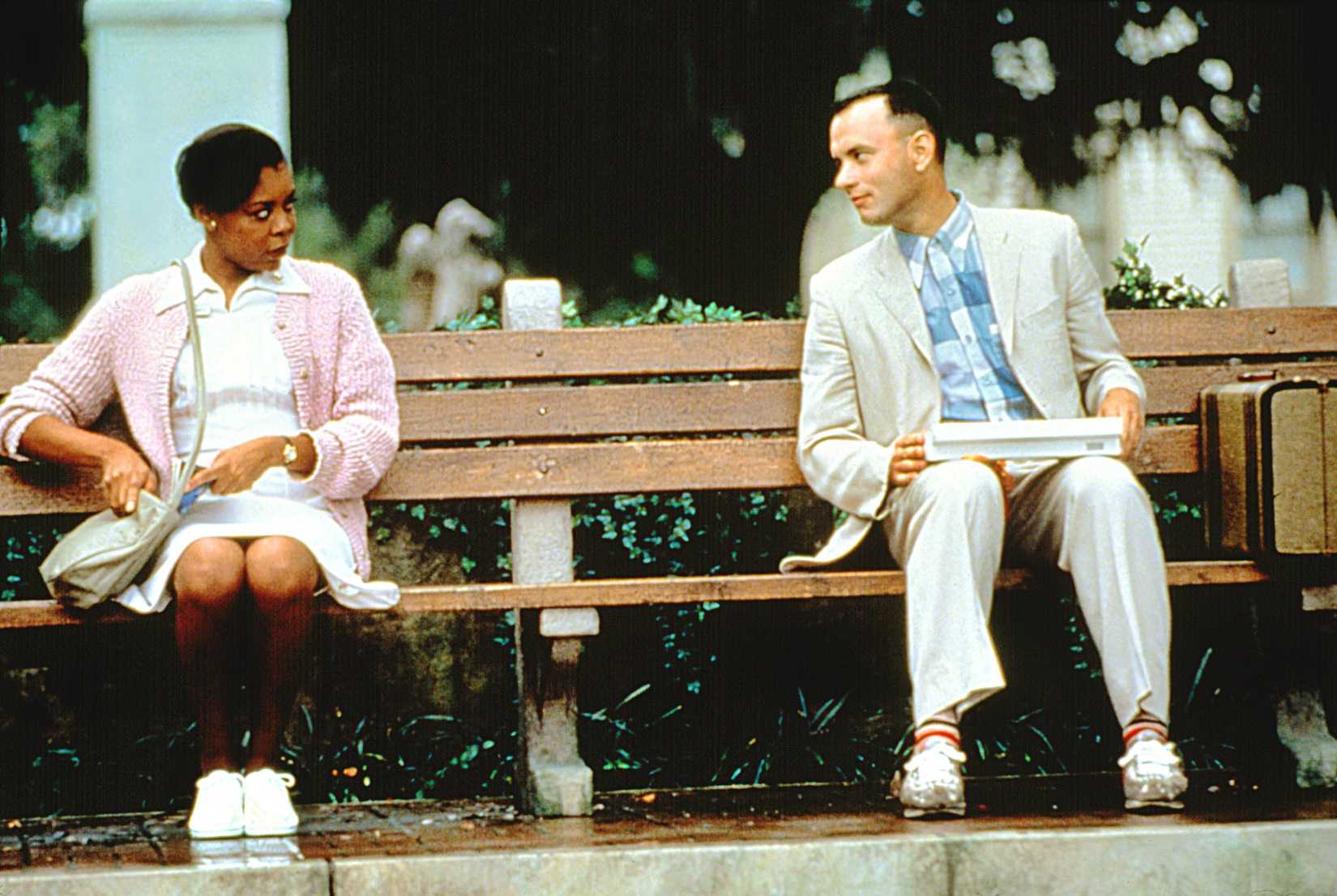 Forrest Gump holding a box of chocolates and talking to a woman.