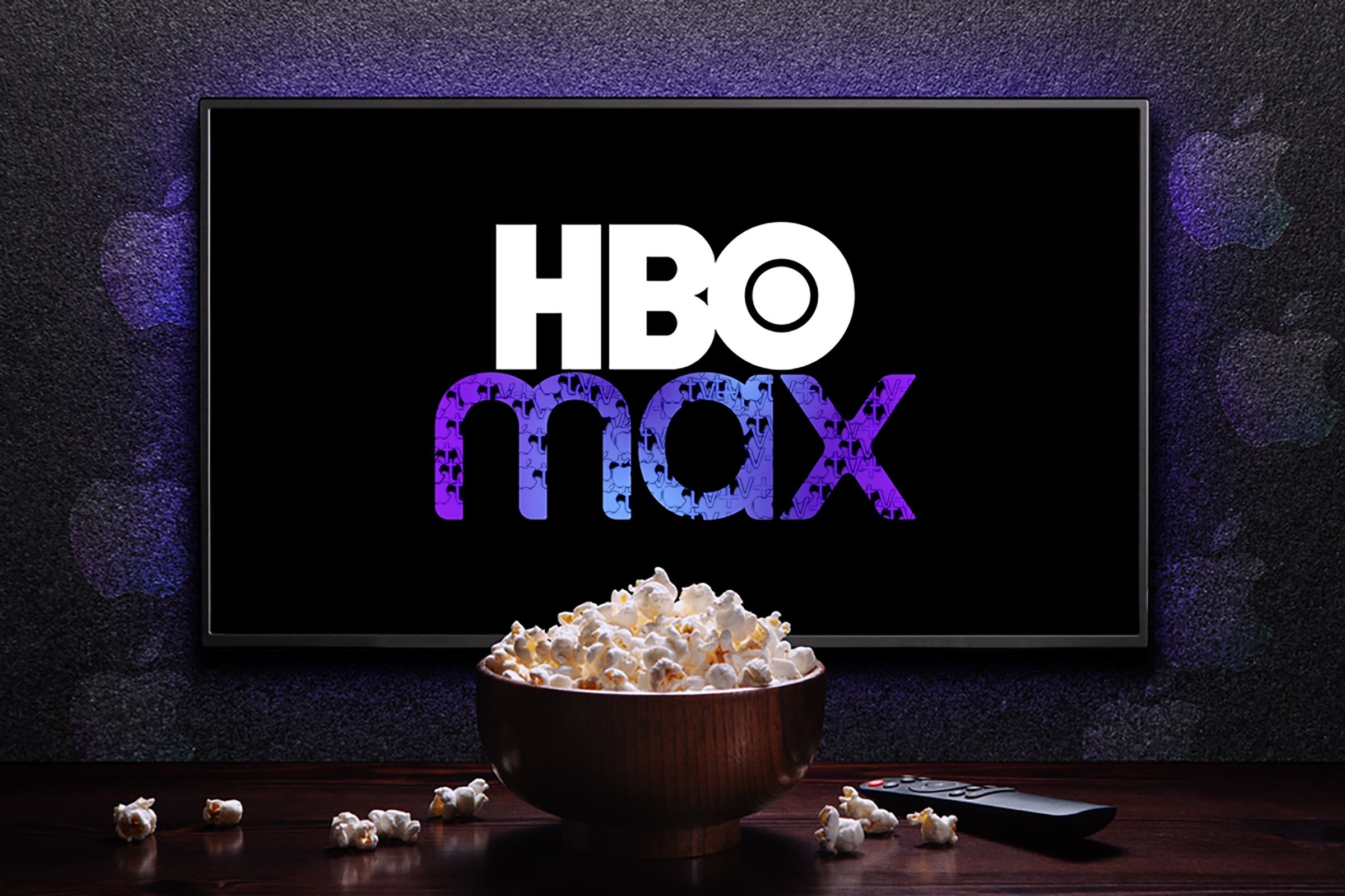 HBO Max logo on TV with popcorn bowl and remote control on the table with Apple TV logos sprinkled on the wall