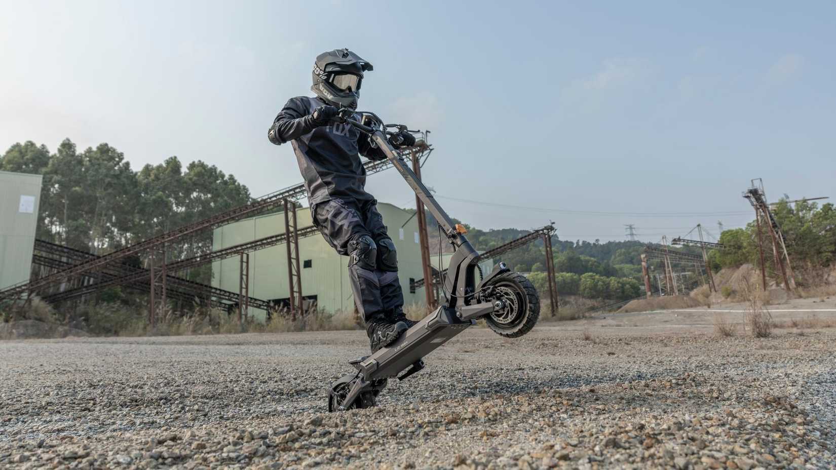 Ausom L2 Max Dual Motor, rider popping a wheelie on gravel terrain