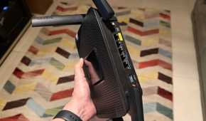 Hand holding a Linksys EA8300 router showing the ports on the back side