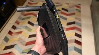 Hand holding a Linksys EA8300 router showing the ports on the back side