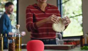 A Google Home Speaker in Berry, sitting on a kitchen counter.