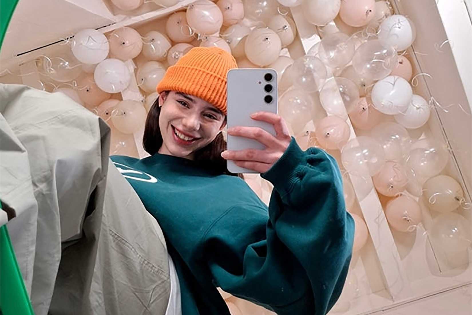 Jeune femme souriante en prenant un selfie avec son smartphone Samsung Galaxy A35.