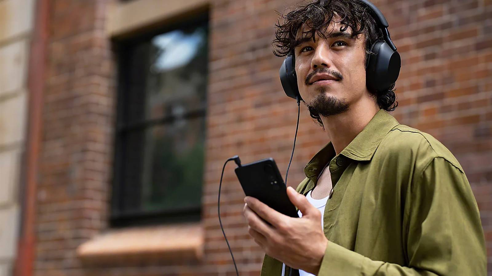 A man walking down the street with wired headphones connected to to a Sony Xperia smartphone.