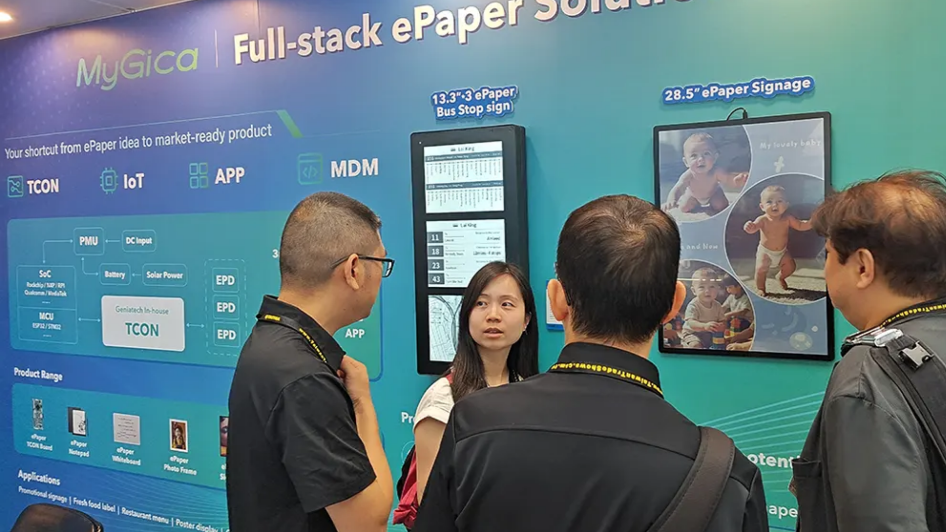 A group of professionals reviewing MyGica's full-stack ePaper solutions and digital signage displays at an exhibition booth.