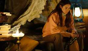 Annie in a sweater sitting on a bed thinking in Paradise.