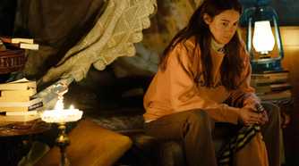 Annie in a sweater sitting on a bed thinking in Paradise.