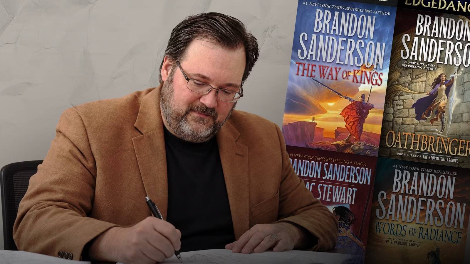 Brandon Sanderson writing at a dest beside several of his fantasy novels