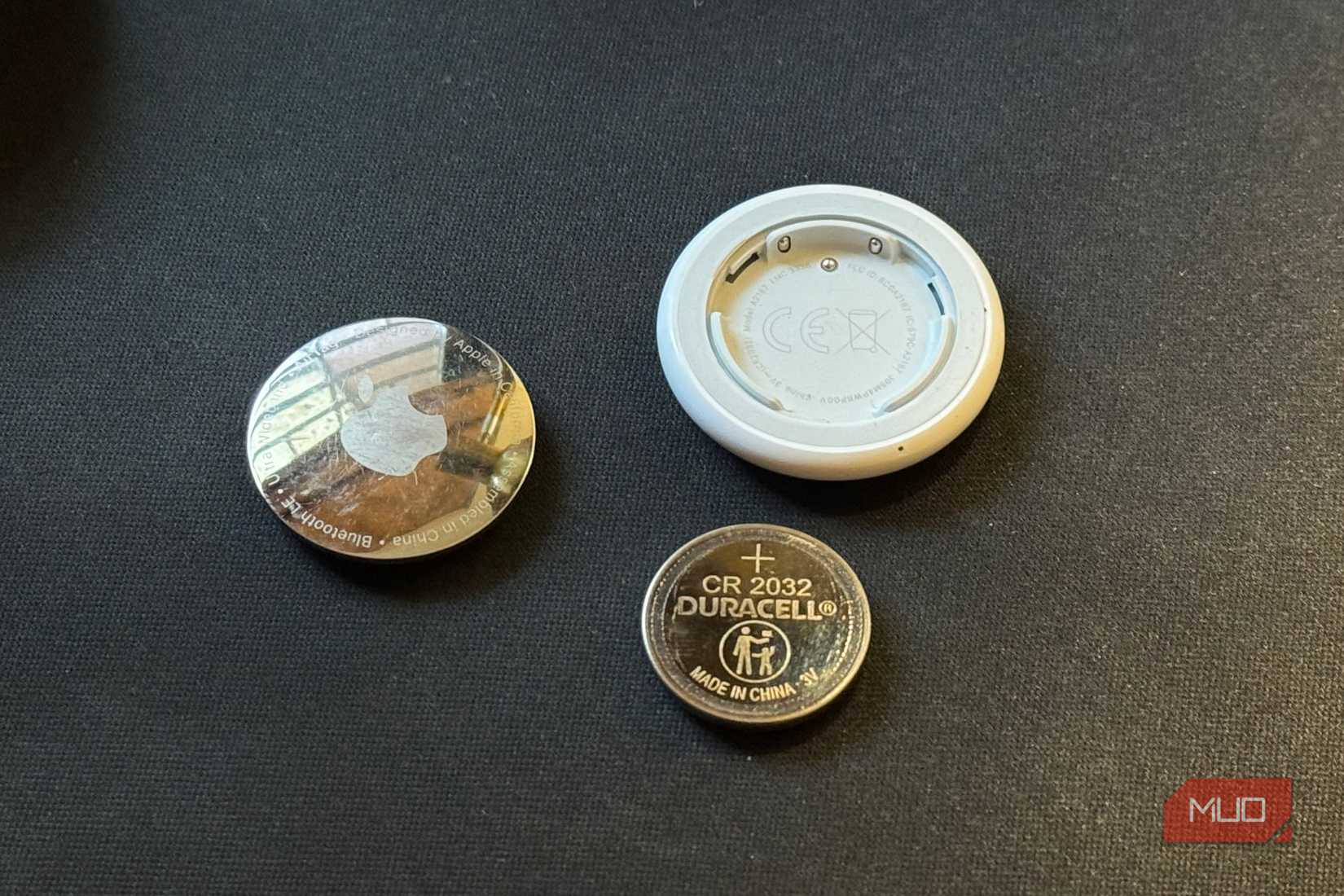 A disassembled AirTag placed on a black mat along with its CR 2032 cell