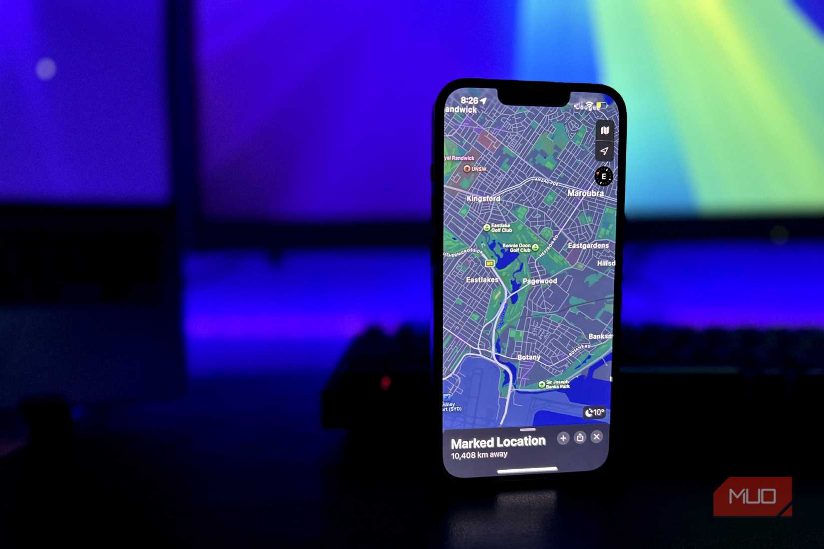 iPhone with the Maps app open and a MacBook and a monitor in the background