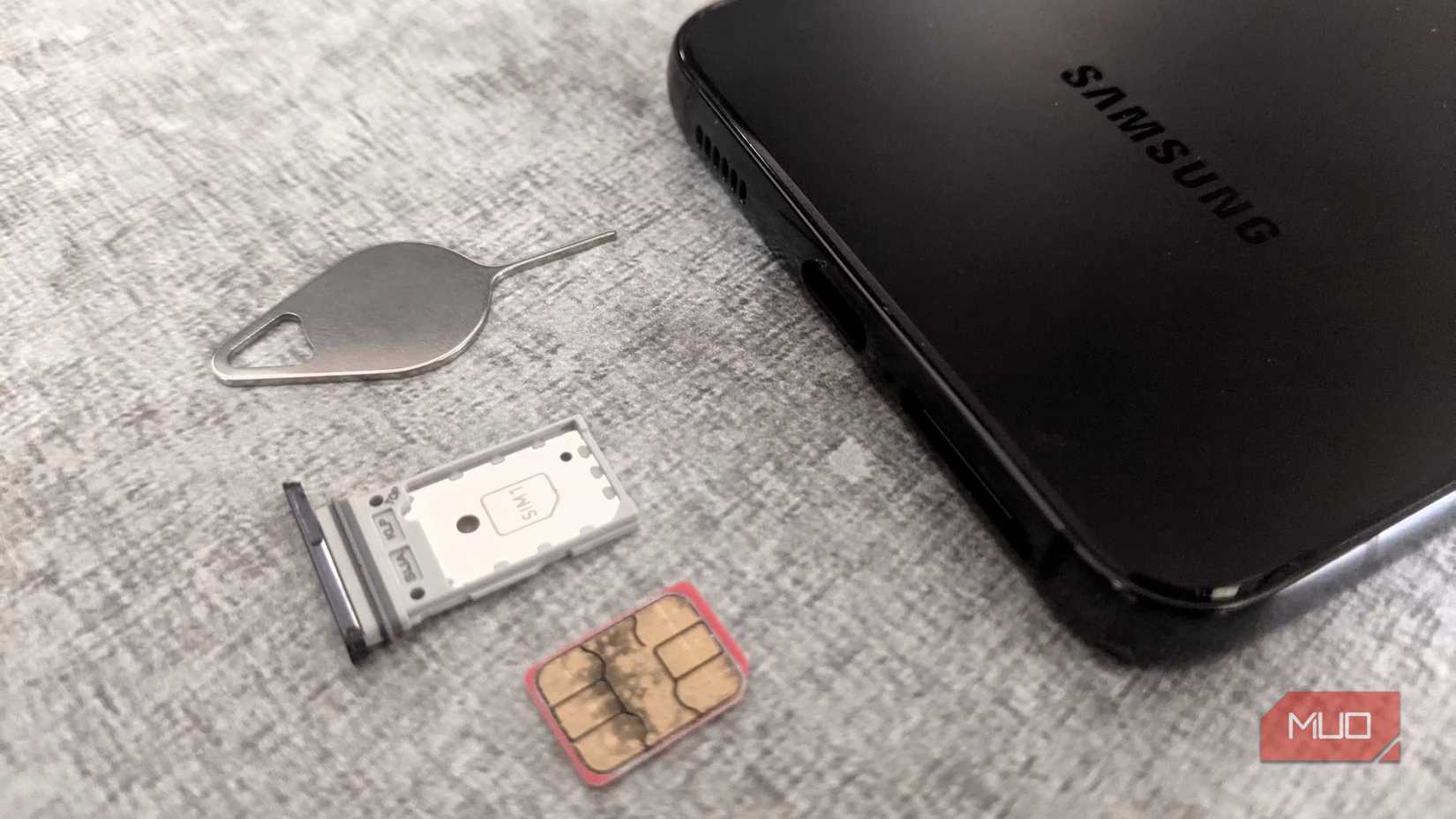 A Samsung smartphone, its SIM card tray, and a SIM ejector tool lying on a flat surface.