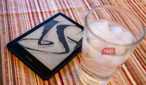 Amazon Kindle Paperwhite Signature Edition next to a glass of water.