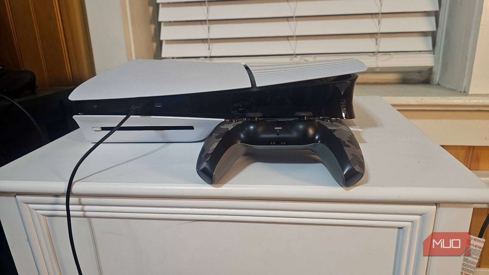 A PlayStation 5 on a white end table with a camo-colored DualSense controller