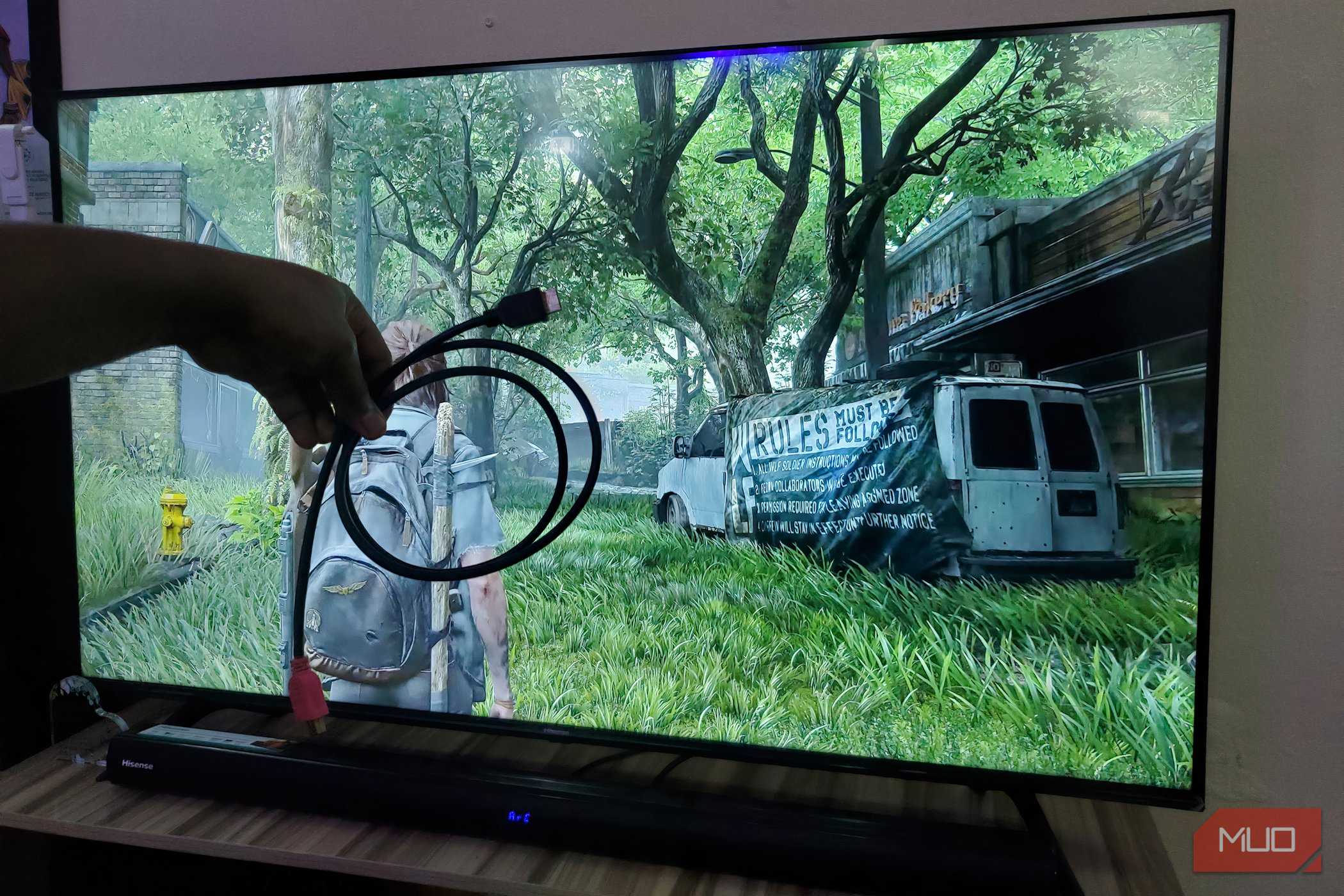 A hand holding an HDMI cable in front of a TV screen.