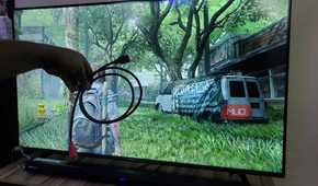 A hand holding an HDMI cable in front of a TV screen.