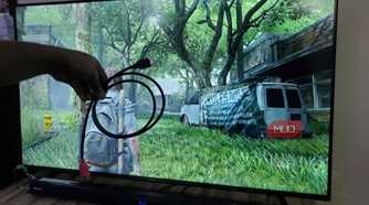 A hand holding an HDMI cable in front of a TV screen.