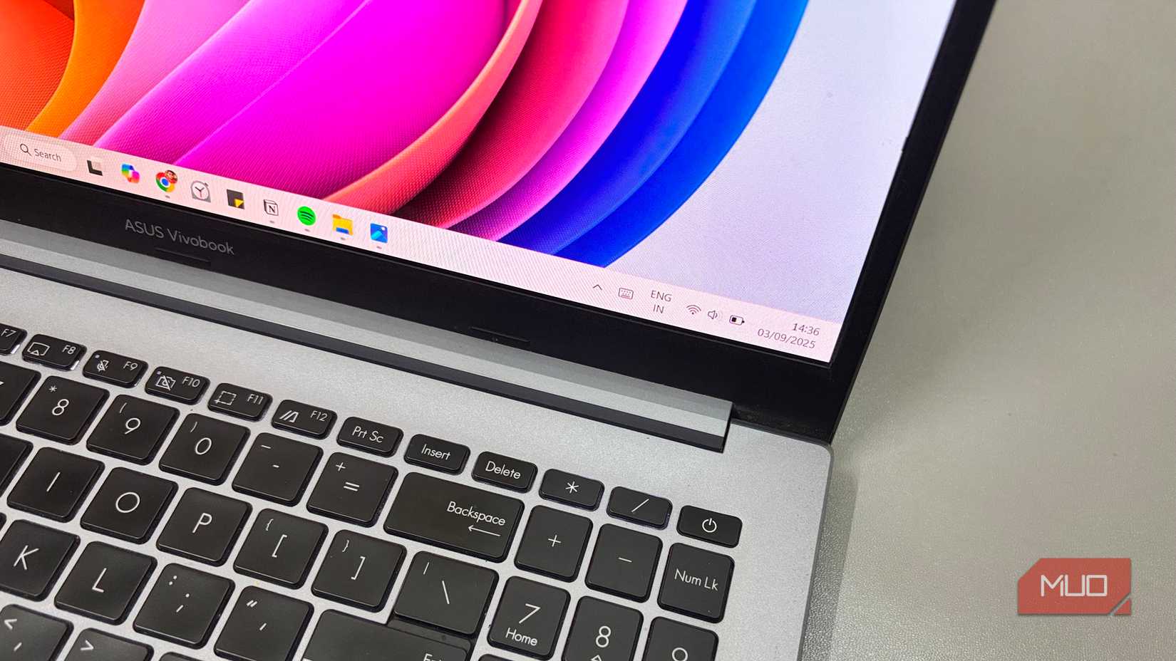 ASUS Vivobook laptop showing Windows 11 desktop with taskbar and colorful screen background.