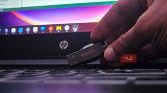 Human hand holding a sandisk USB drive on a laptop keyboard