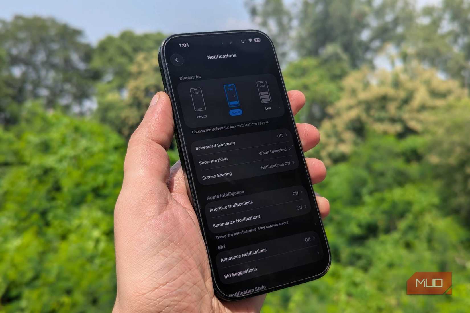 iPhone 16 Pro in hand with Notification settings on screen and greenery in the background