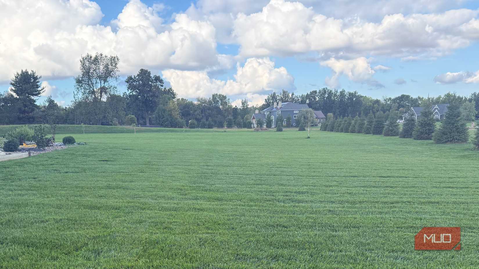 large area of green grass with trees and clouds in background