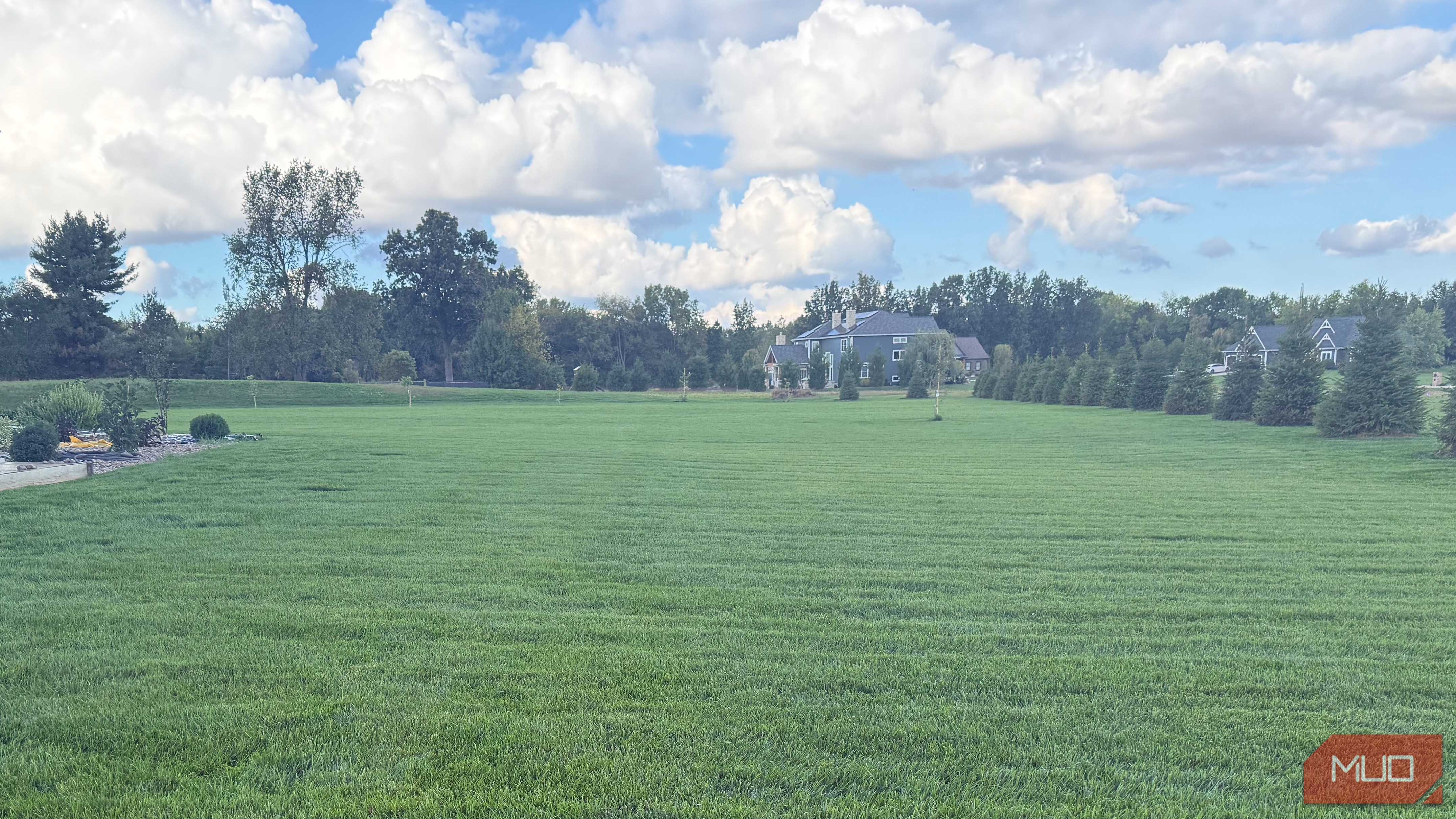 large area of green grass with trees and clouds in background