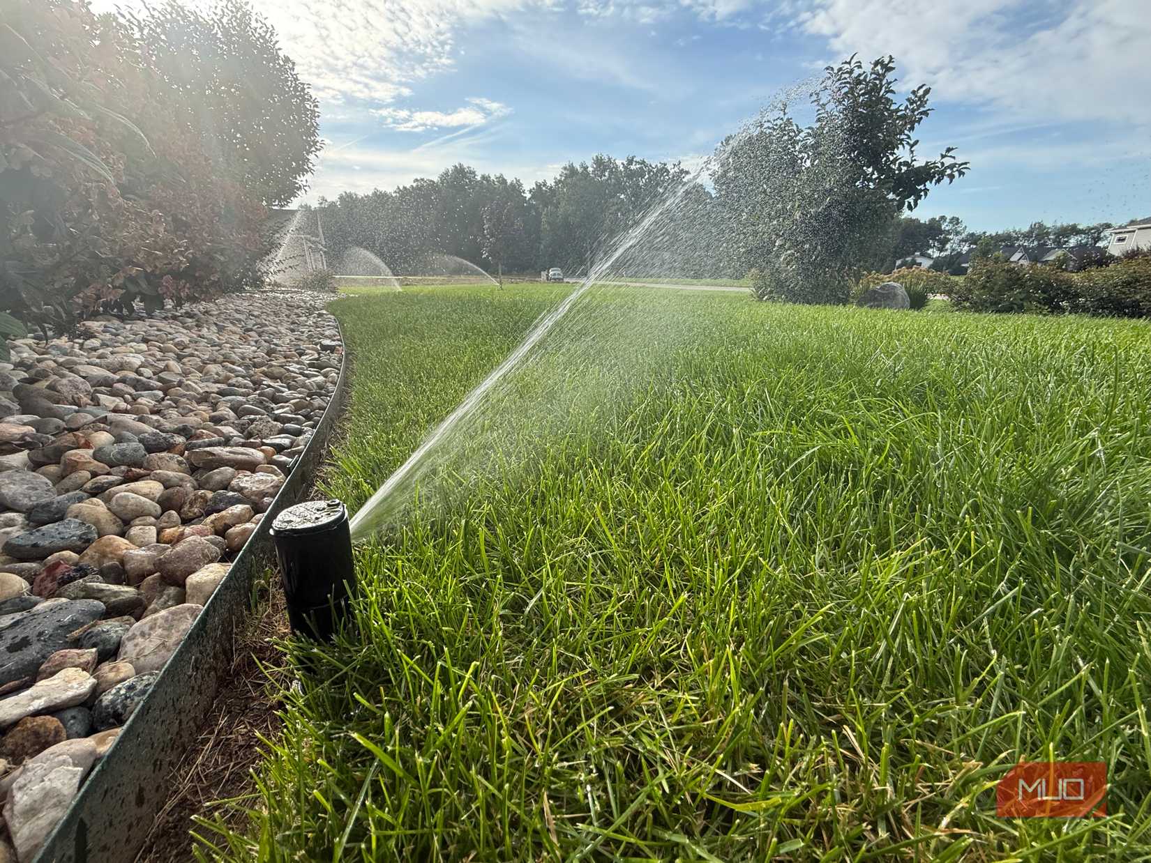 Sprinklers spraying water in yard next to landscape river rock bed