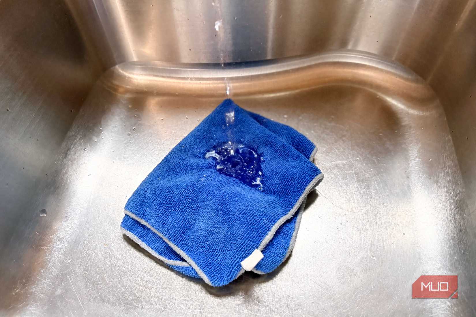 A blue microfiber cloth in a sink being sprayed with water.
