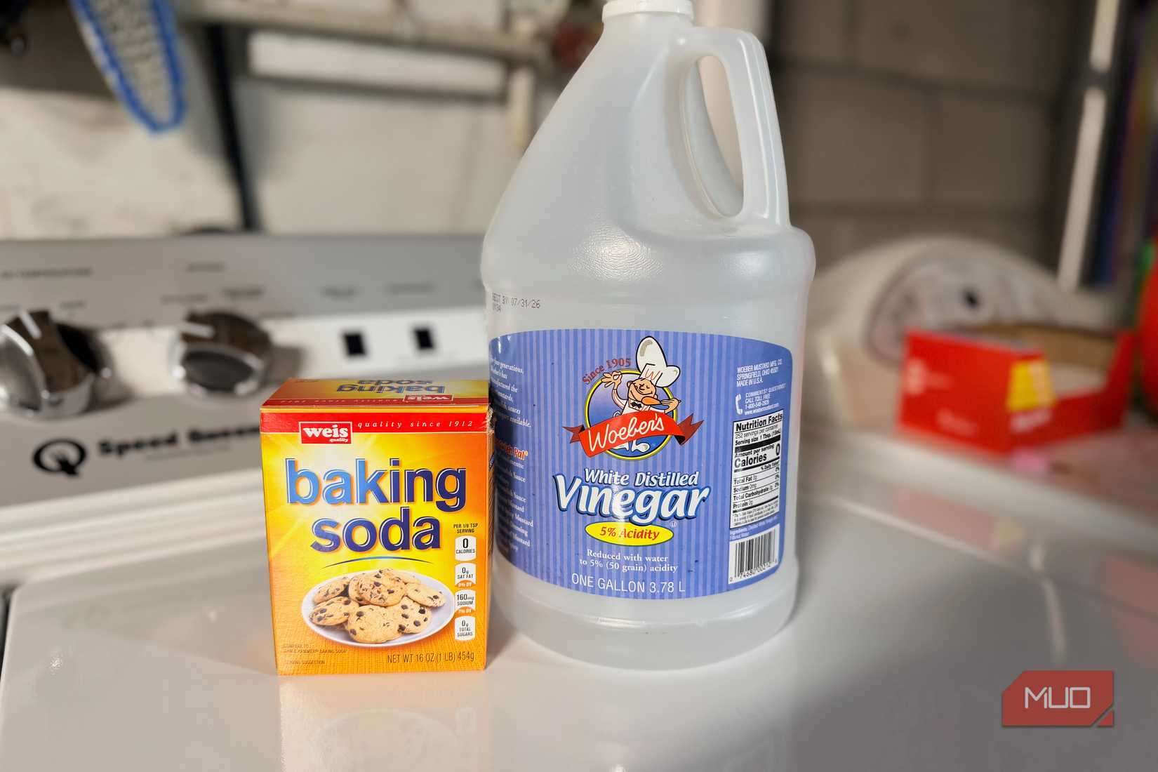 A box of baking soda and white vinegar bottle sitting on the top of a washing machine. 
