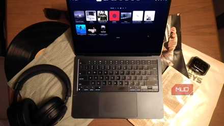 جهاز MacBook يقوم بتشغيل الموسيقى على مكتب مليء بأقراص الموسيقى المضغوطة وأسطوانة الفينيل وسماعات الرأس