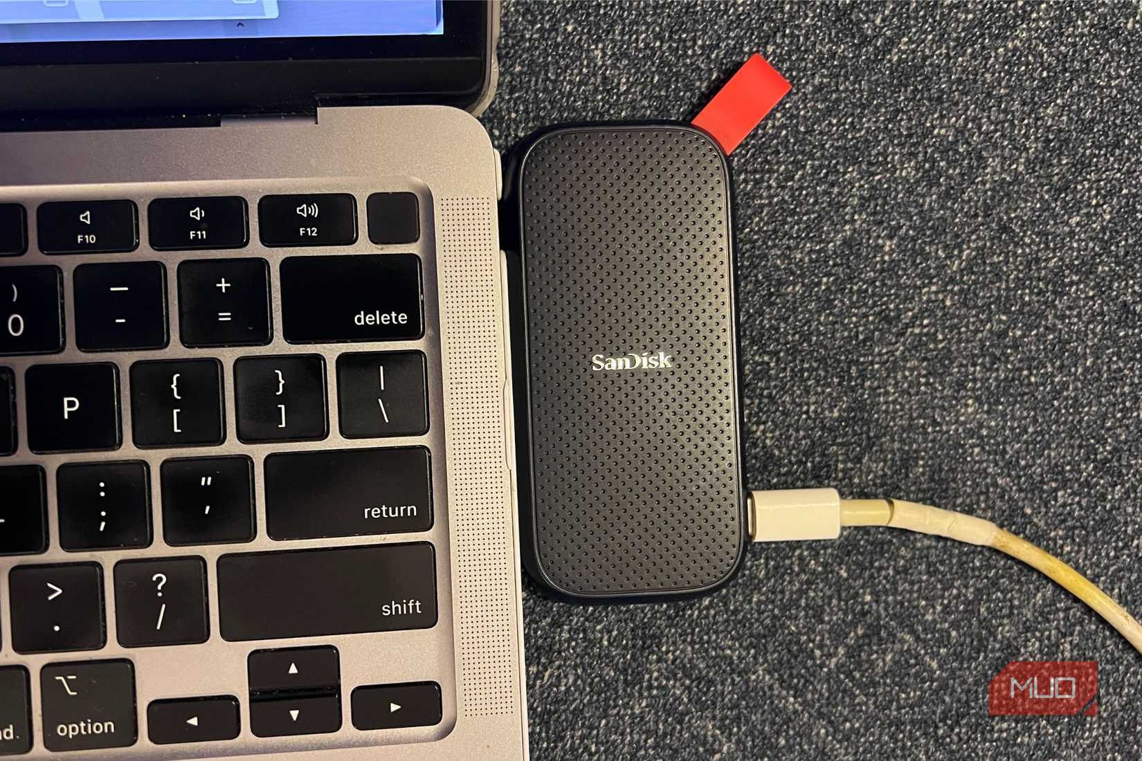 A SanDisk SSD placed next to a MacBook keyboard showing delete among other keys