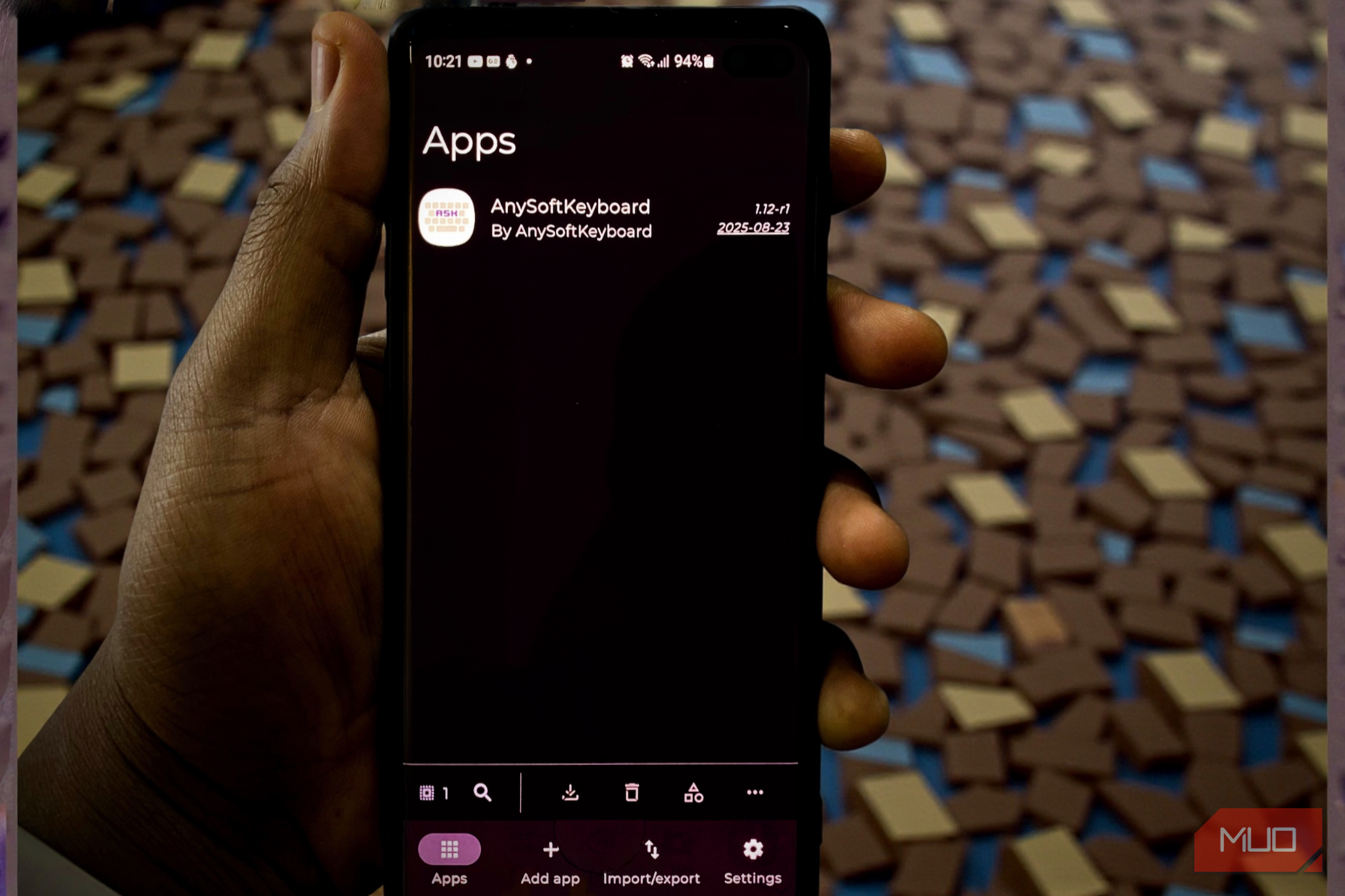 A hand holding a smartphone displaying the Obtainium app dashboard with AnySoftKeyboard listed-1