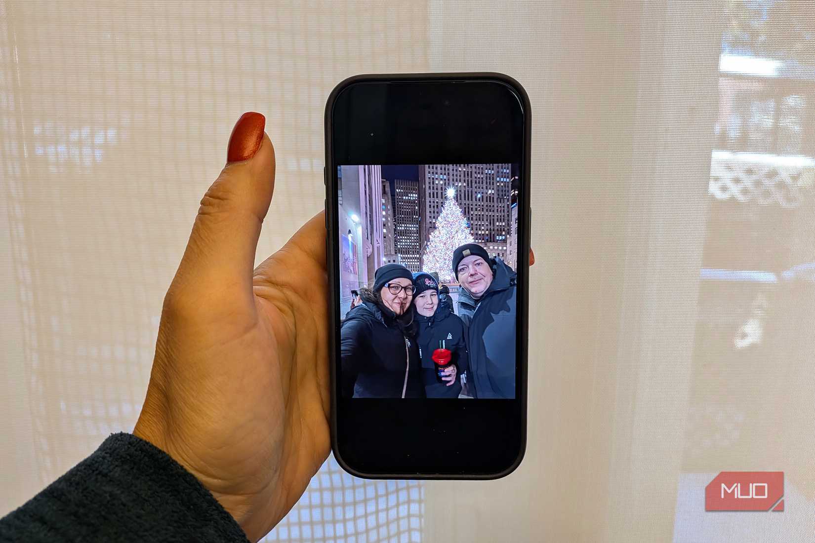Una mano sosteniendo una foto de tres personas paradas frente a un árbol de Navidad afuera.