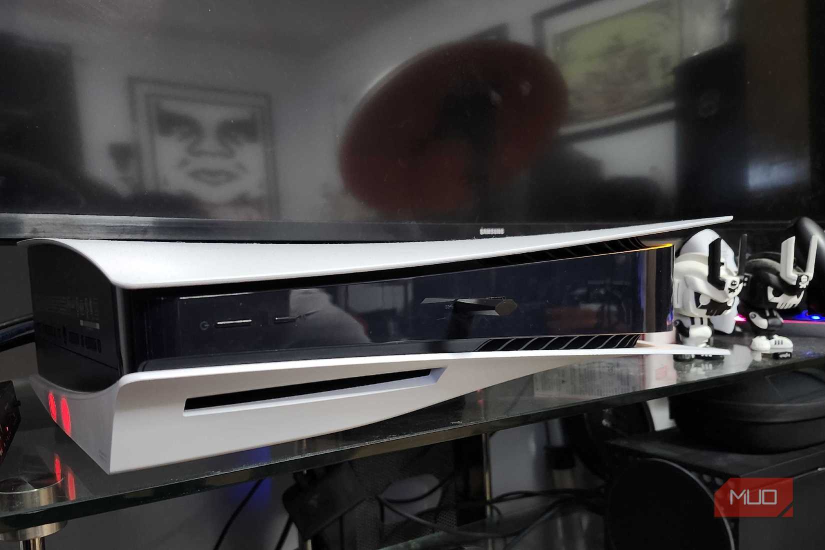 A PlayStation 5 resting below a smart TV on a glass entertainment center