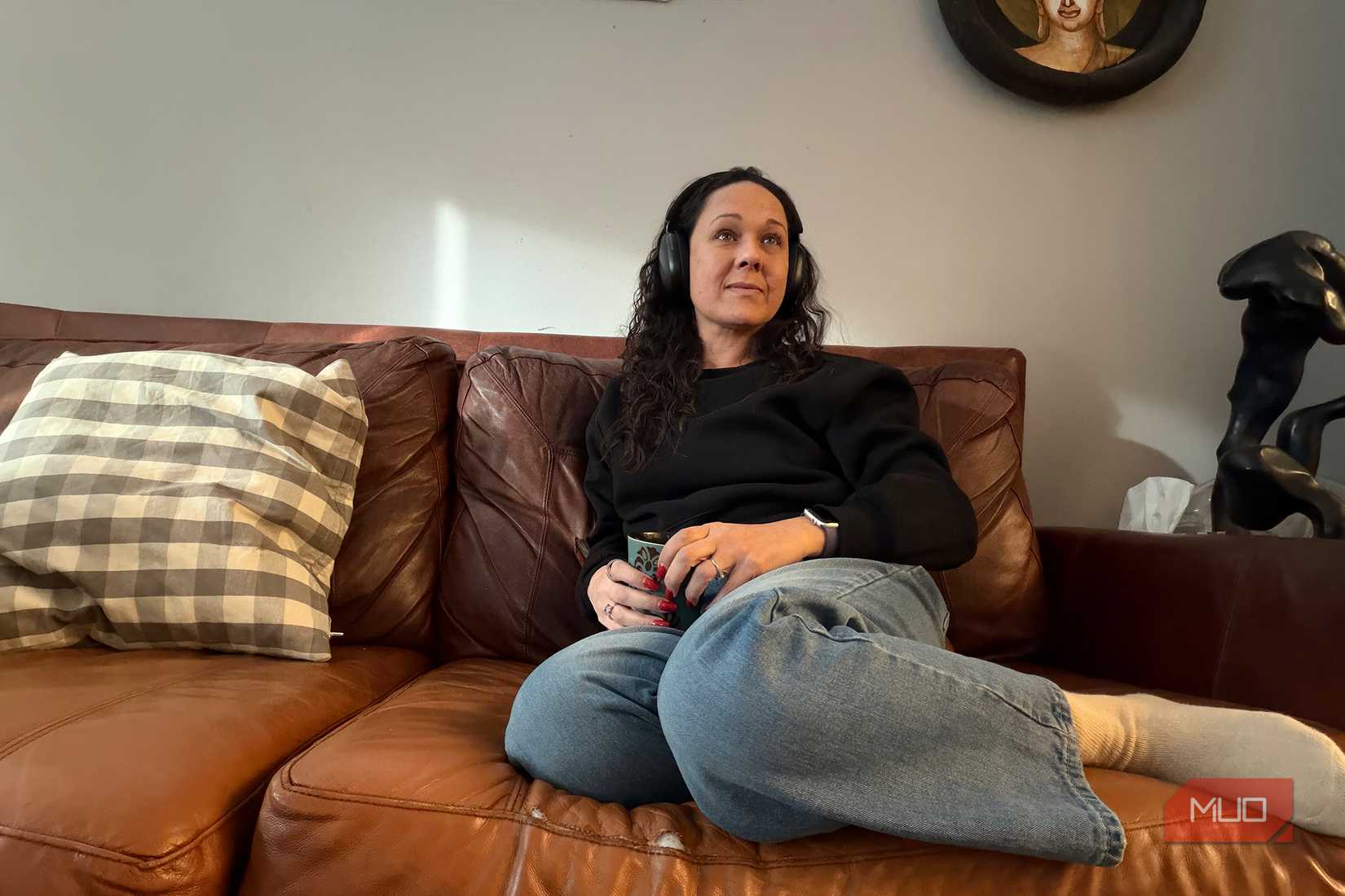 A woman sitting back on the couch watching TV with headphones on.
