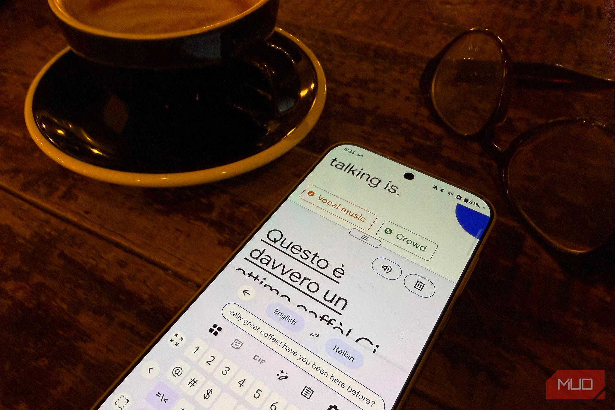 A phone on a table beside a cappuccino and glasses showing a translation.