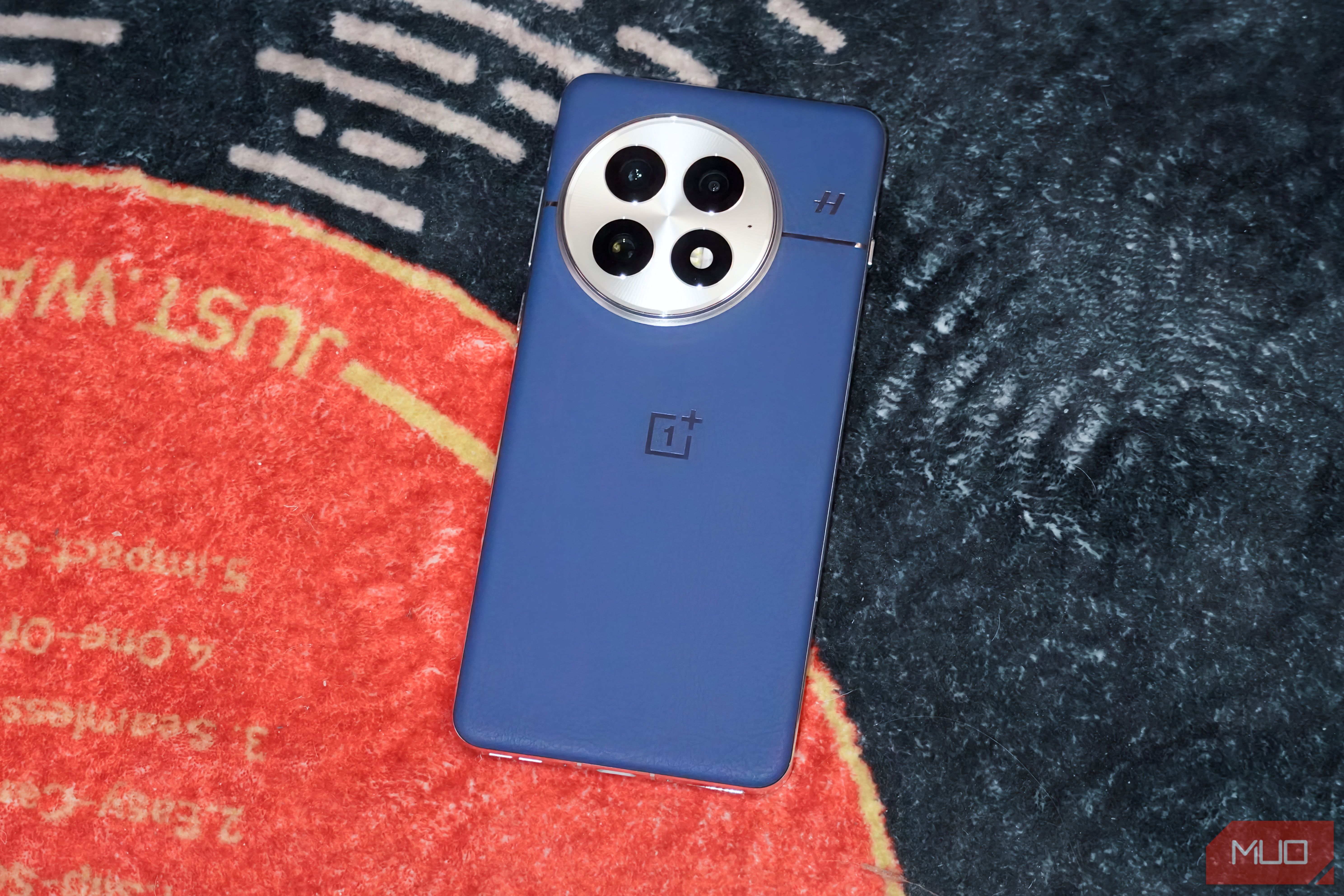 The blue OnePlus 13 on a vinyl-themed rug.