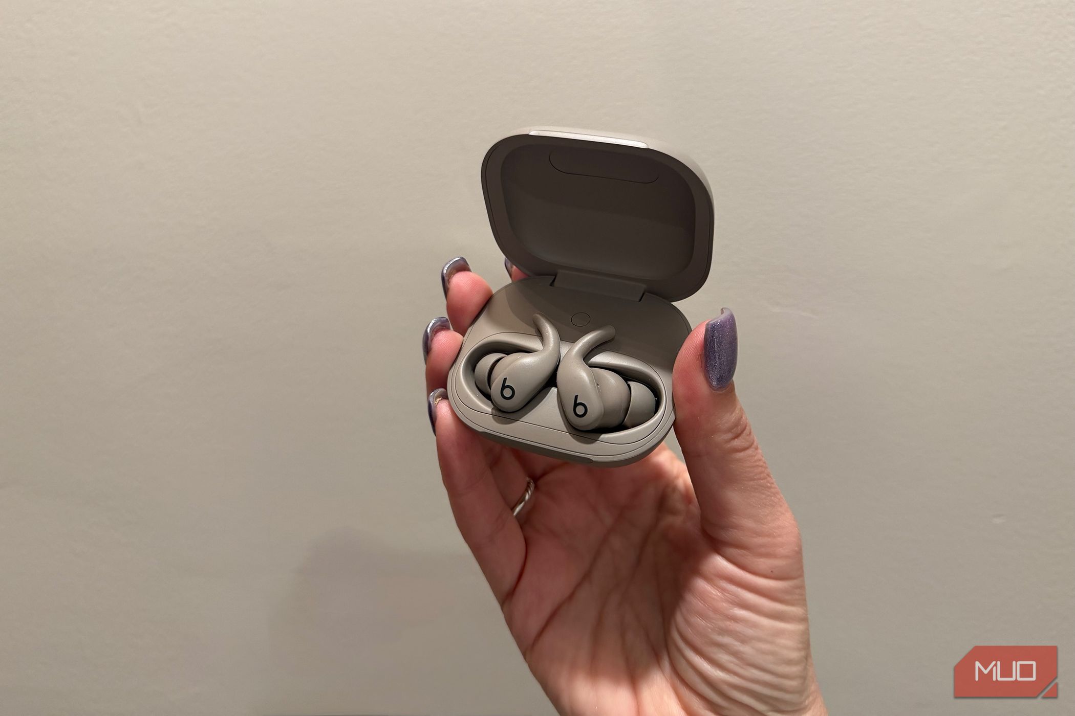 Powerbeats Fit open in their case in hand being held up by a wall.