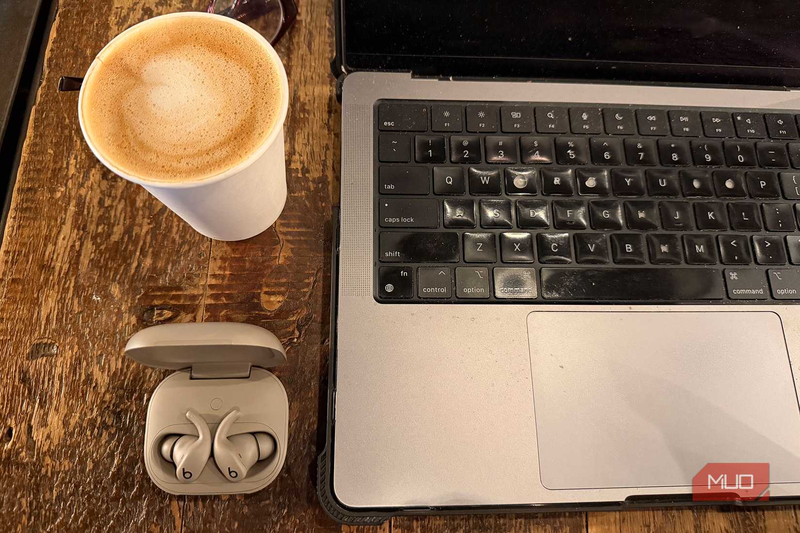 An overhead view of the Powerbeats Fit in the open case with coffee and a laptop.