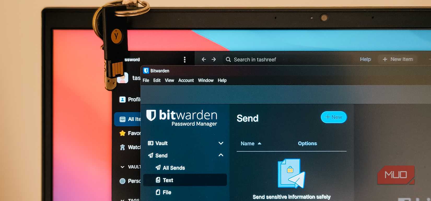 Bitwarden and 1Password apps open in overlapping windows on Windows 11 with a YubiKey dangling on top of the laptop lid.