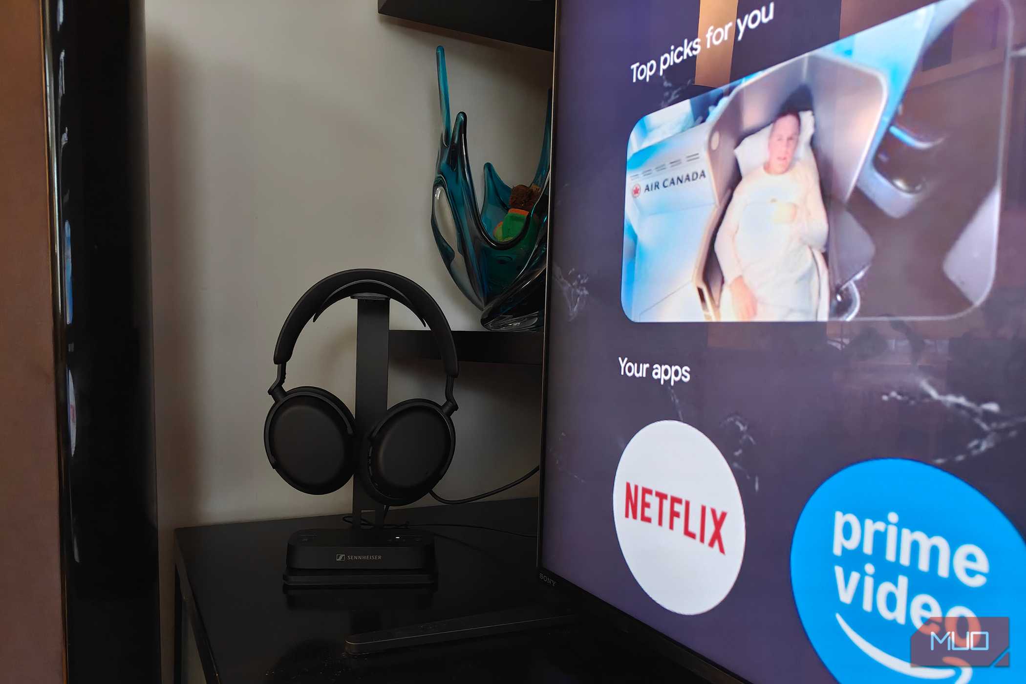 The Sennheiser RS 275 headphones on a stand with the BTA1 Bluetooth transmitter at the base beside a TV.