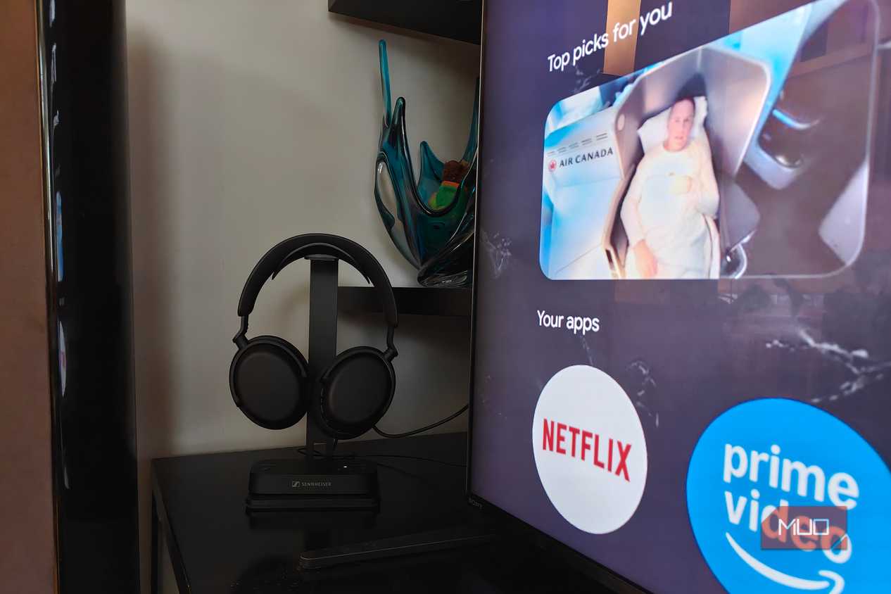 The Sennheiser RS 275 headphones on a stand with the BTA1 Bluetooth transmitter at the base beside a TV.