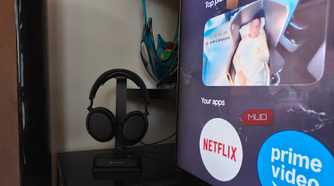 The Sennheiser RS 275 headphones on a stand with the BTA1 Bluetooth transmitter at the base beside a TV.
