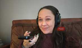 A woman holding a remote and wearing the Sennheiser RS 275 headphones.