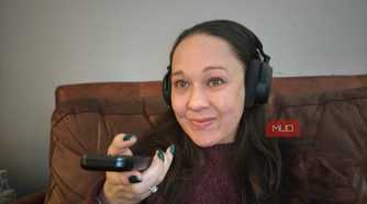 A woman holding a remote and wearing the Sennheiser RS 275 headphones.