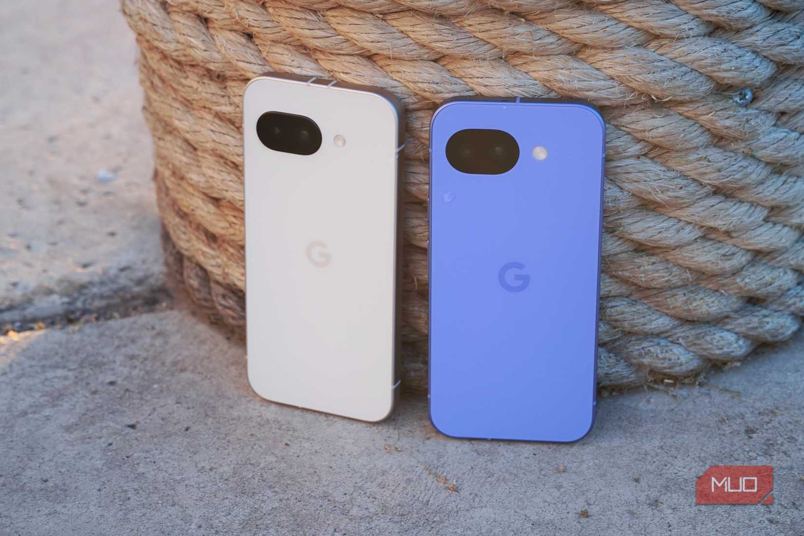 The Google Pixel 9a (left) beside the Pixel 10a (right) leaning against a dock post.