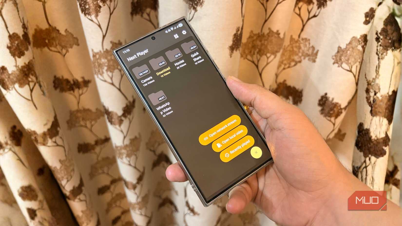 Hand holding an Android phone running Next Player video player with folders and playback options visible