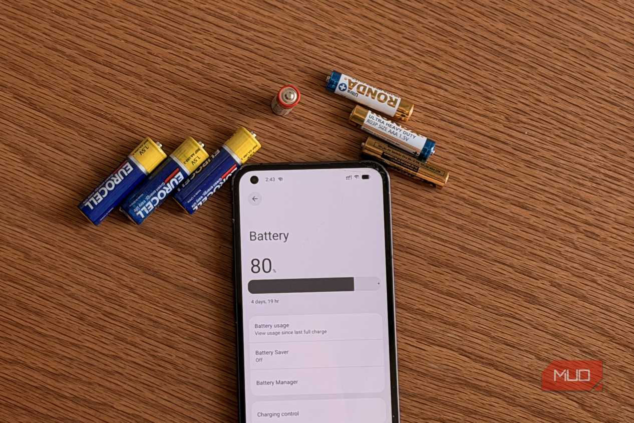 AA and AAA batteries next to an Android phone showing the battery settings